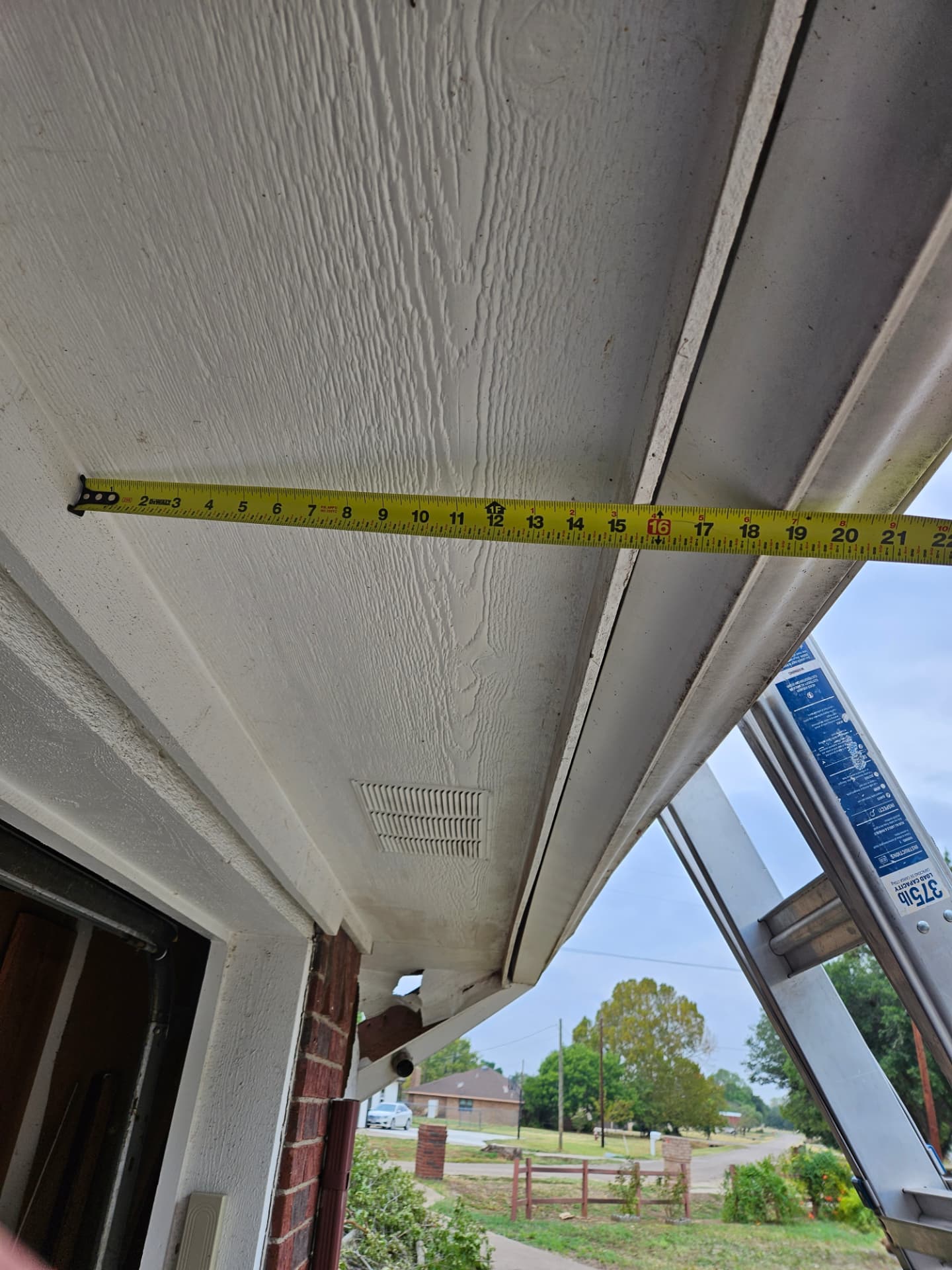 Measuring a louvered soffit vent and damaged eave corner on a Johnson County brick home