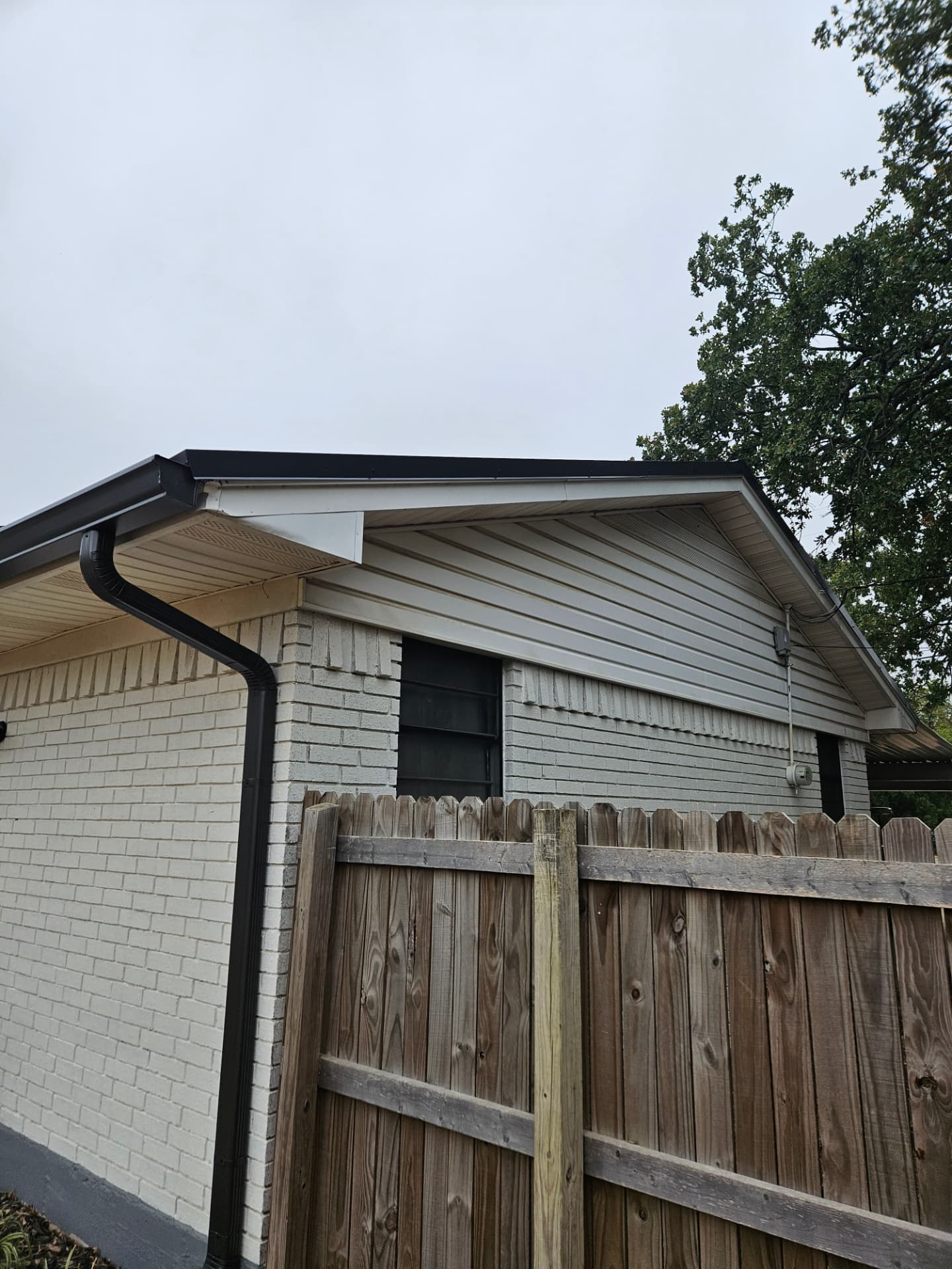 Black seamless gutters and downspout running the corner of a painted brick home in Johnson County