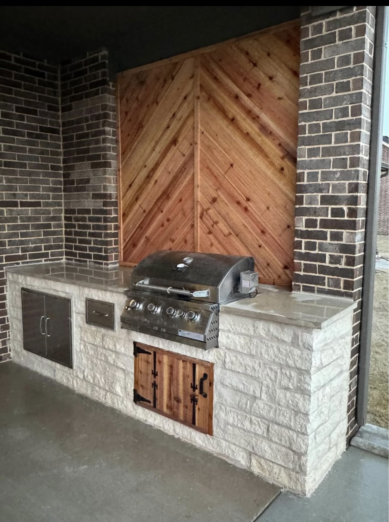 W2 Construction built in grill island with stone base and cedar accent wall on a covered Johnson County patio